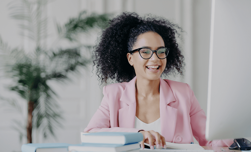 Imagem de uma mulher negra, com o cabelo apanhado, a sorrir enquanto olha para o ecrã de um computador portátil